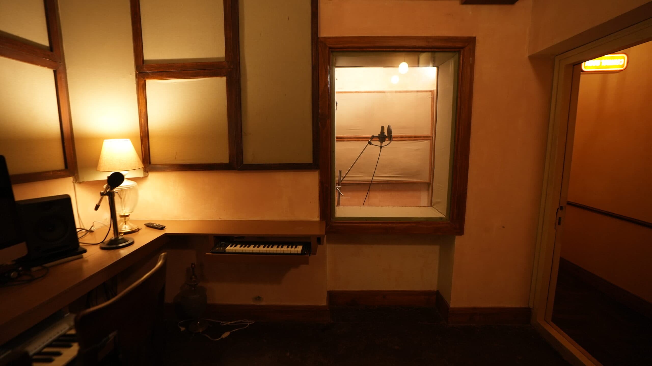 Composition desk with a MIDI keyboard, monitor speakers and a window looking into the booth