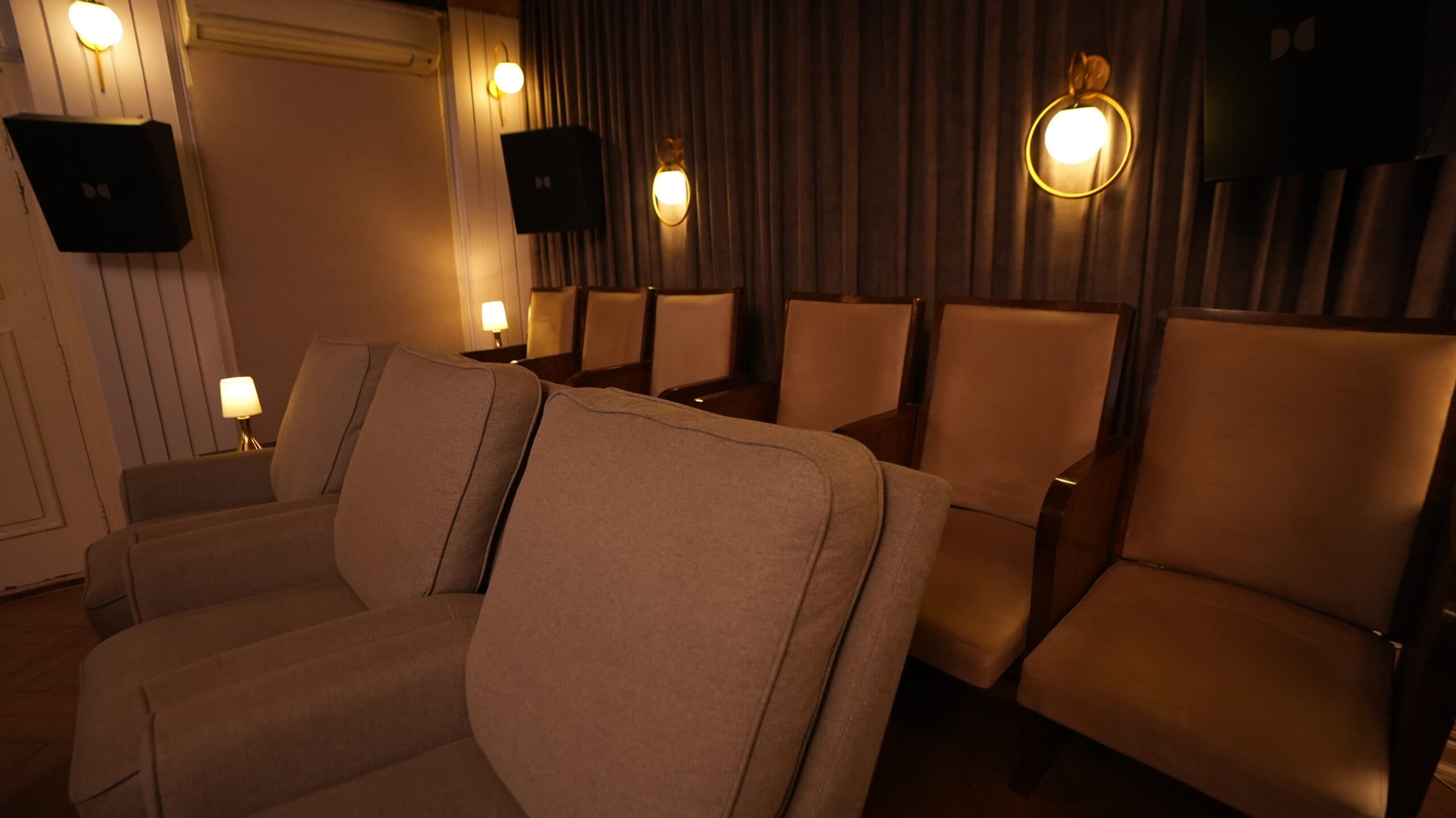 Rows of upholstered theatre seats lit by brass wall sconces