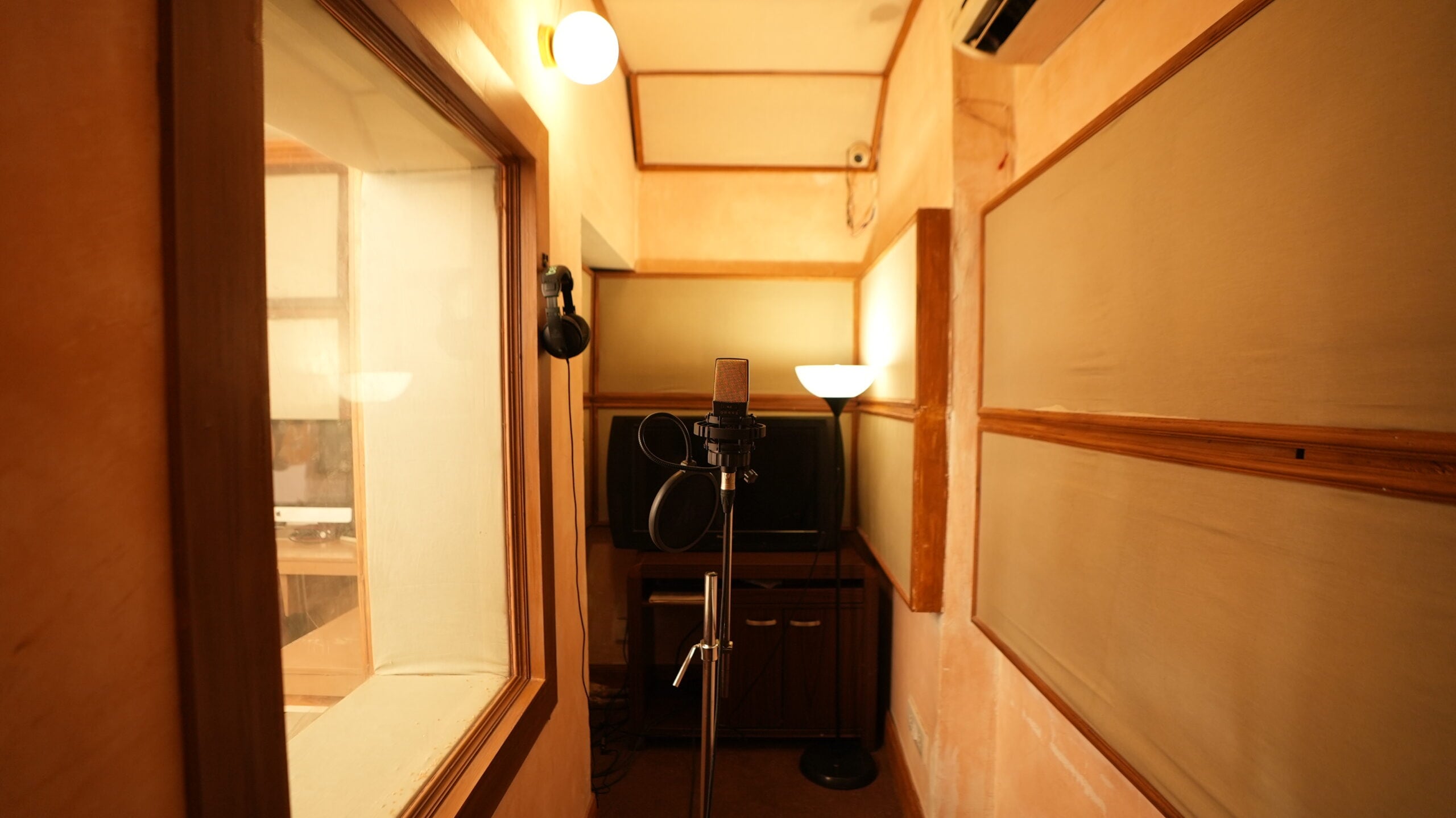 The narrow vocal booth with a large-diaphragm condenser microphone, pop filter and headphones