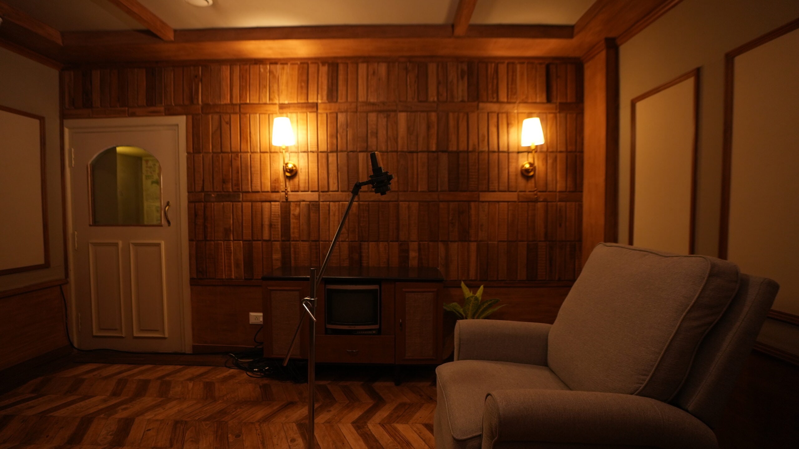 A condenser microphone on a boom stand before a wall of reclaimed timber, lit by two brass sconces, in a recording room at Vistar & Volume Studios