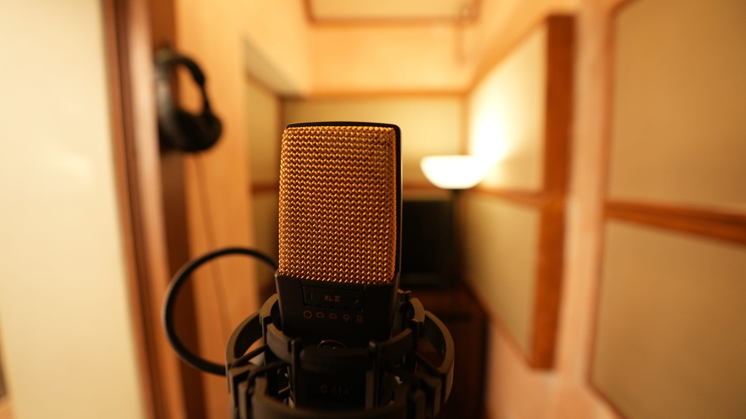An AKG C414 XLII condenser microphone standing in the warm, wood-lined vocal booth
