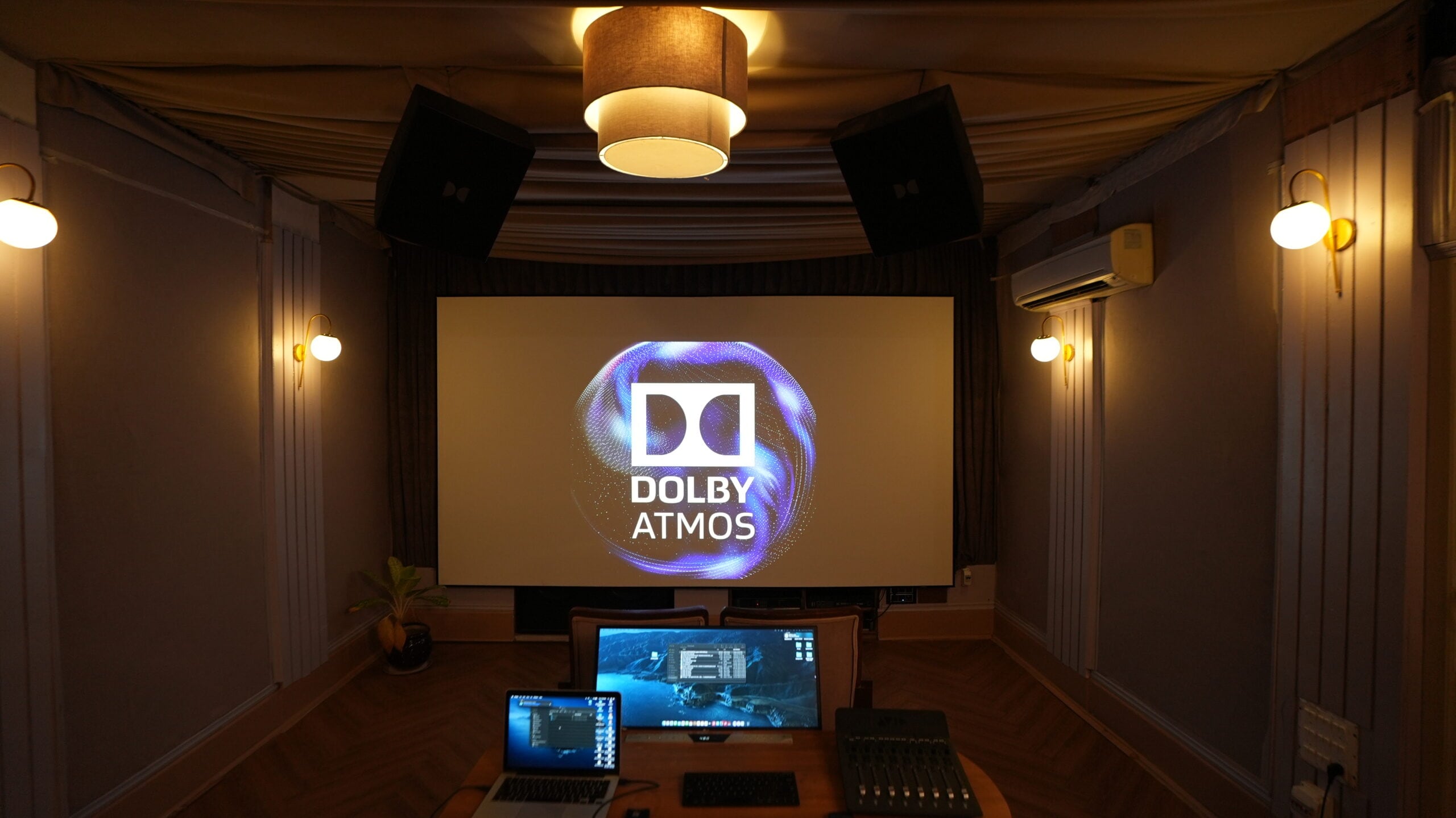 The Atmos mixstage seen over the desk, with two workstation screens and the Dolby logo on the projection screen