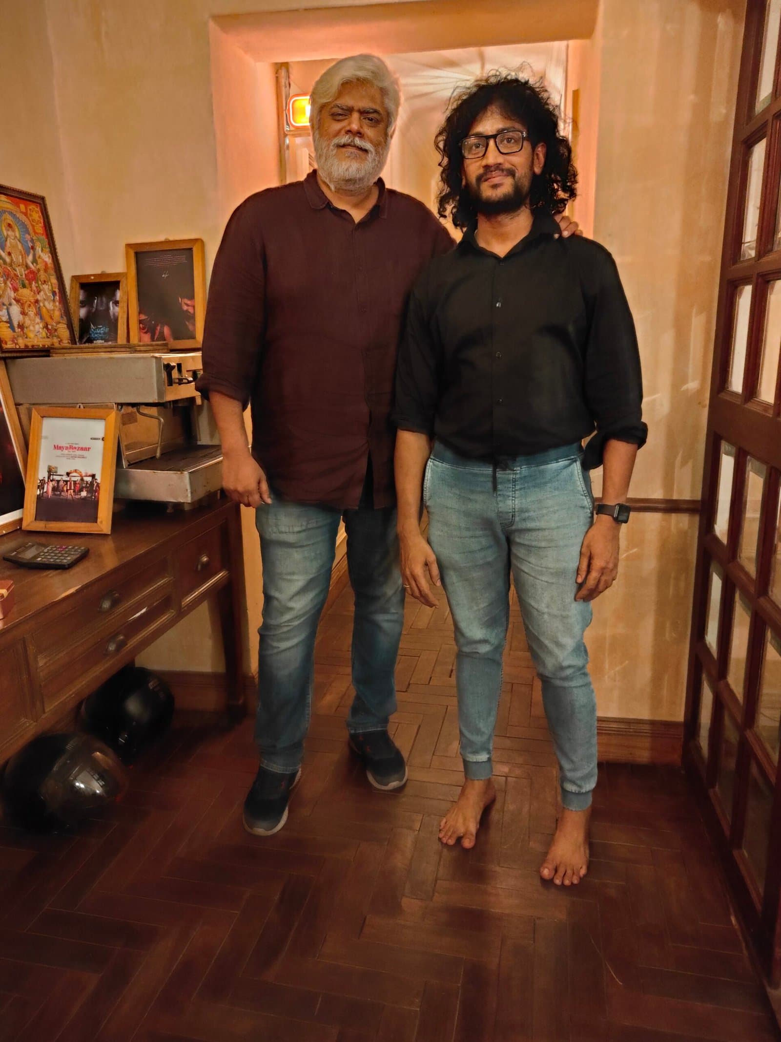 Two collaborators posing by the wood-panelled doors of the studio