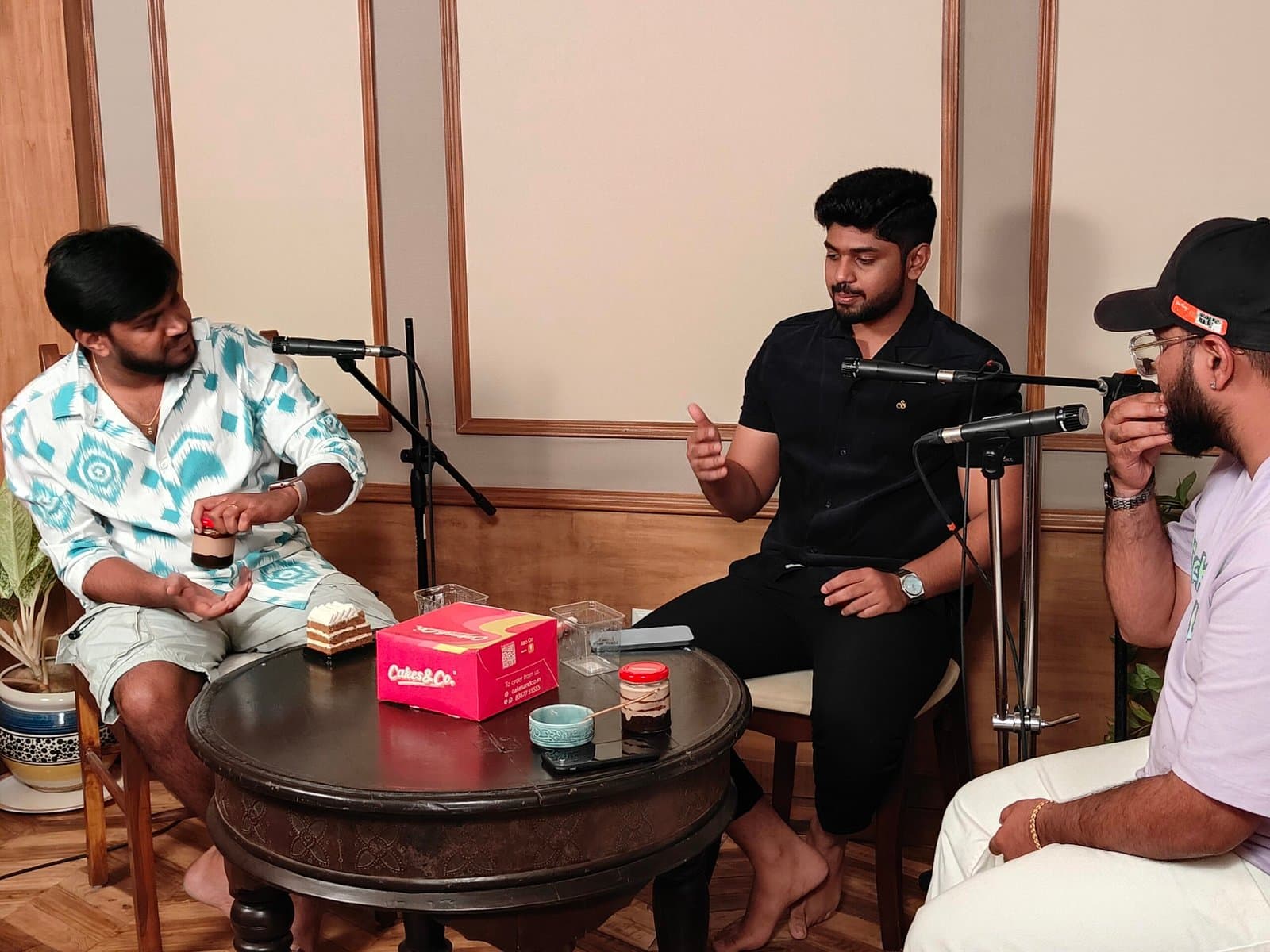 Three podcasters around a coffee table, recording into boom microphones
